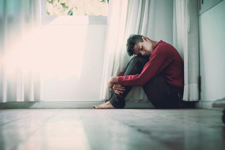 Illustration de la solitude et du repli sur soi chez un jeune homme, assis près d'une fenêtre après un traumatisme.