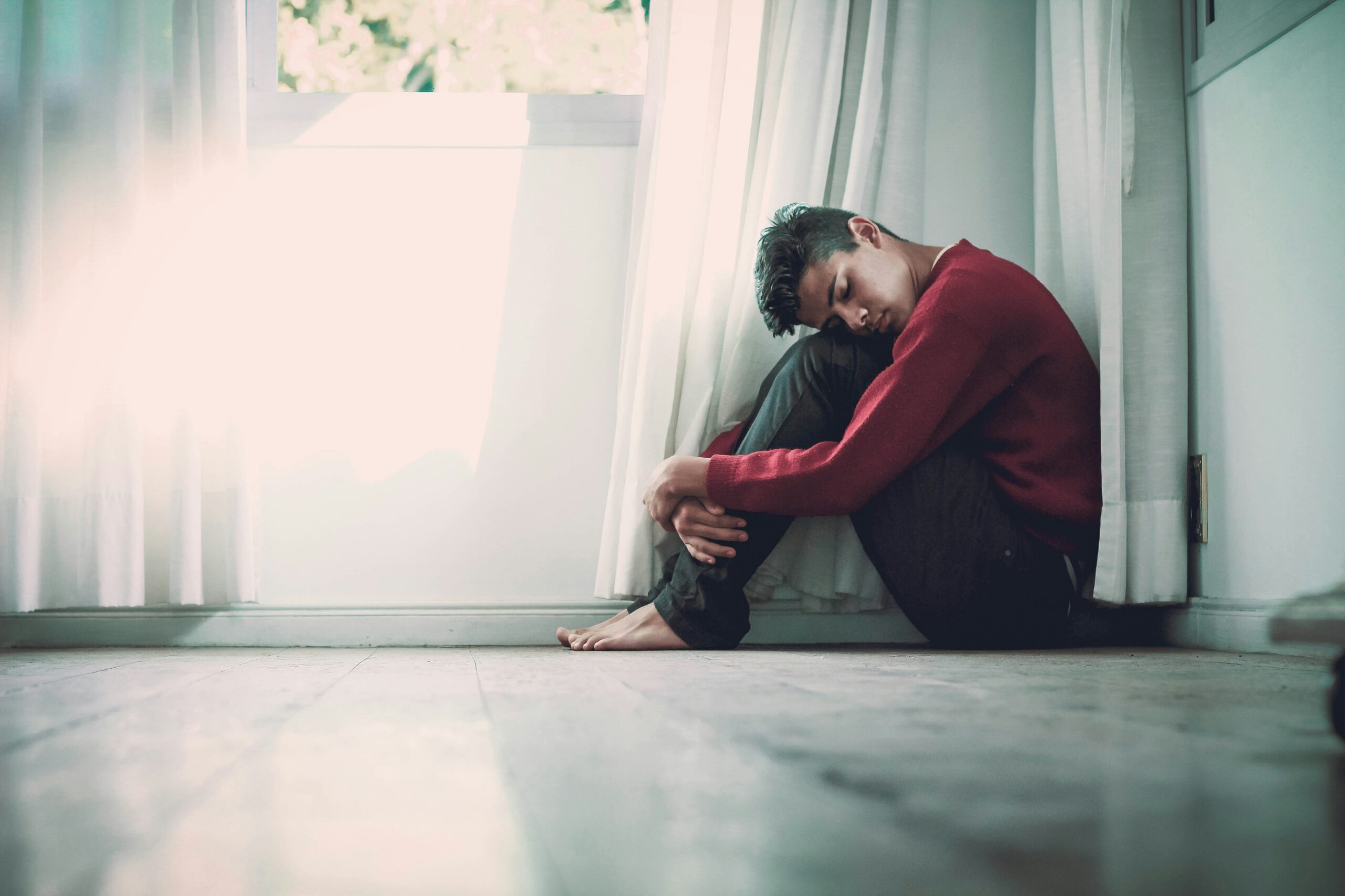 Illustration de la solitude et du repli sur soi chez un jeune homme, assis près d'une fenêtre après un traumatisme.